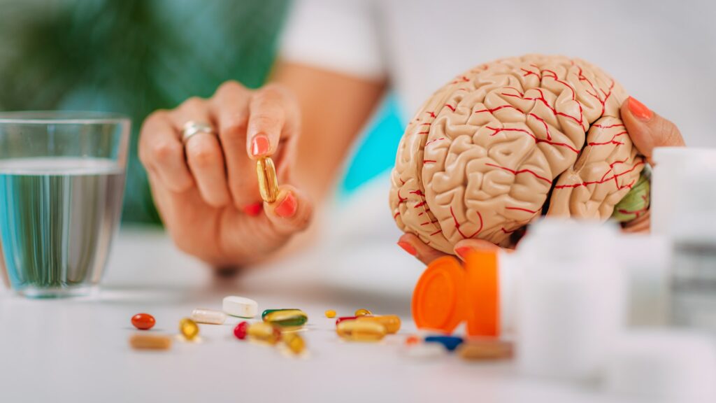 Cognitive improvement or brain supplements. Woman holding a supplement capsule and a model brain.