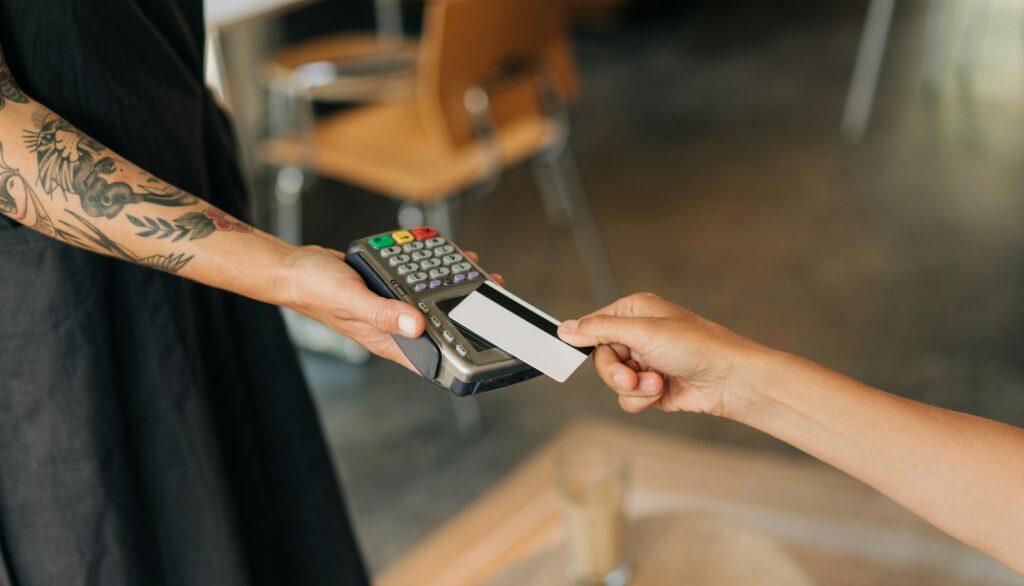 Woman paying with credit card at cafe, close-up of hands with credit card and credit card reader.