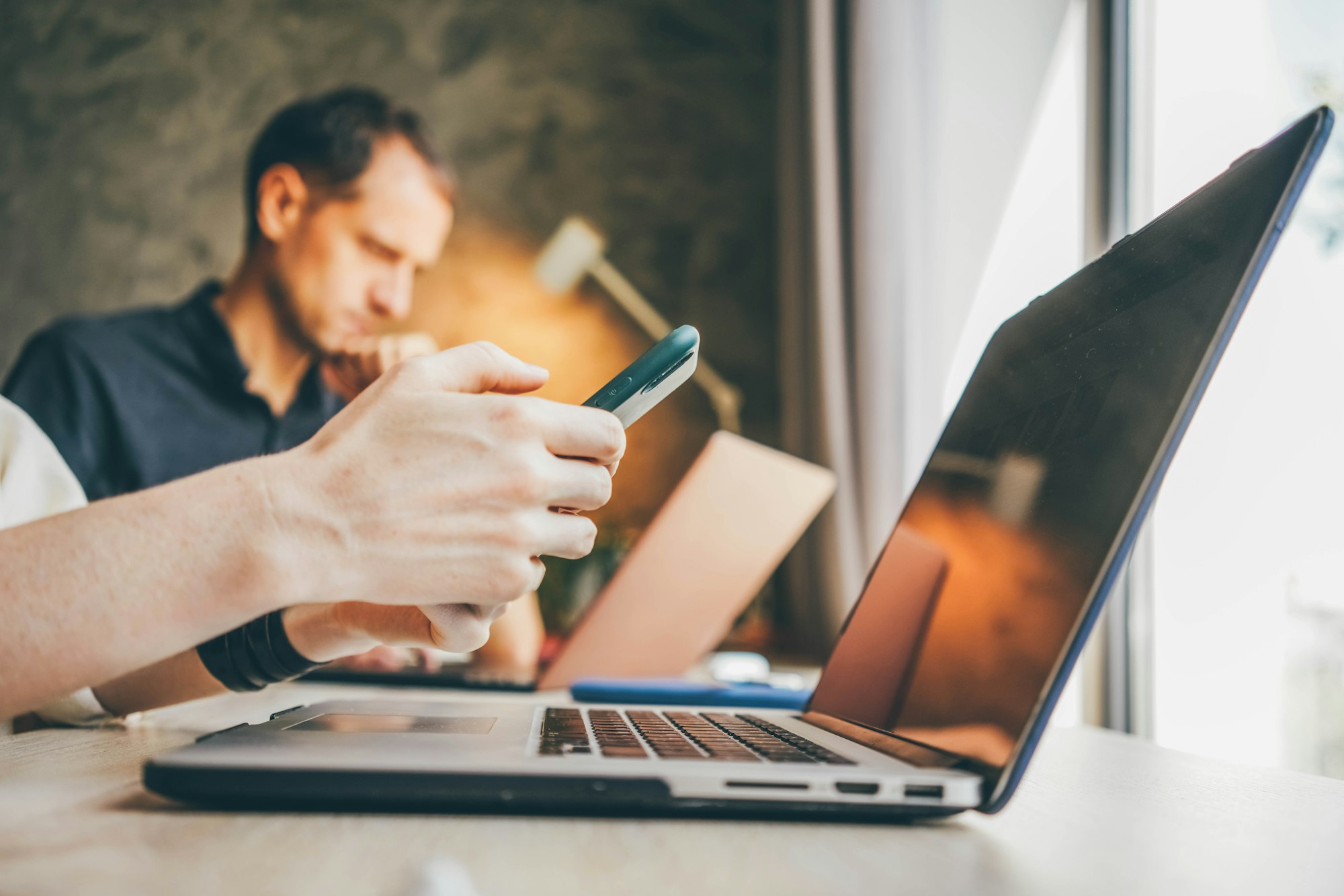 Businesswoman texts message on smartphone working on contemporary laptop