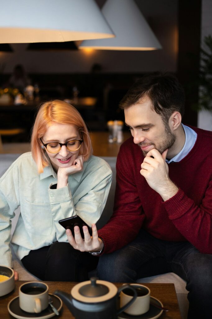 People, communication and dating concept - a young couple communicates in a cafe and looks into a sm