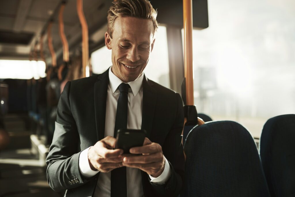 Smiling young businessman reading text messages during his morning commute