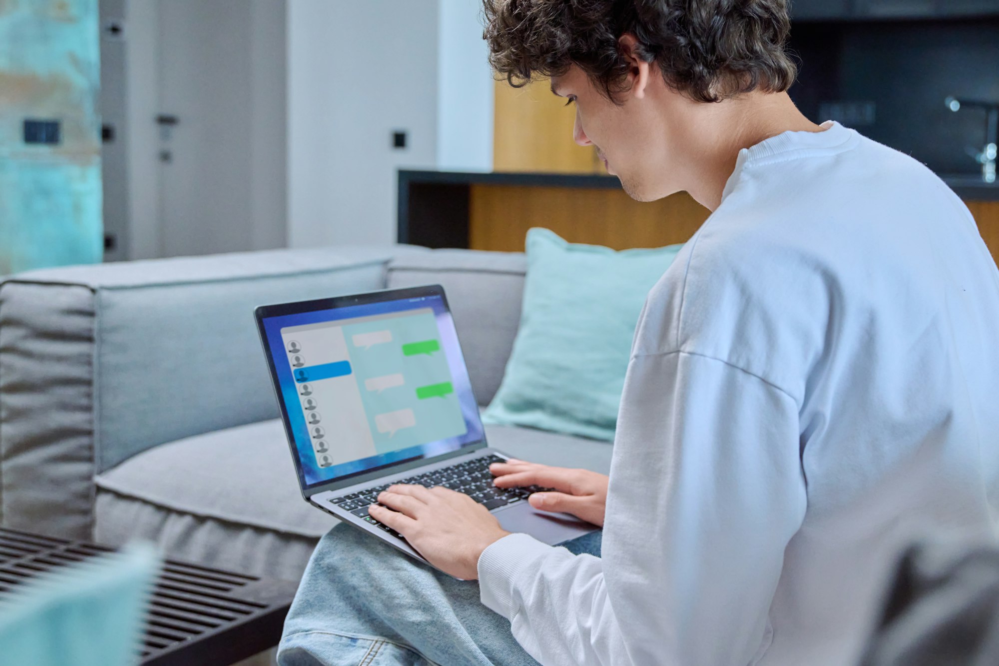 Young male using laptop for chat, sitting resting at home on sofa