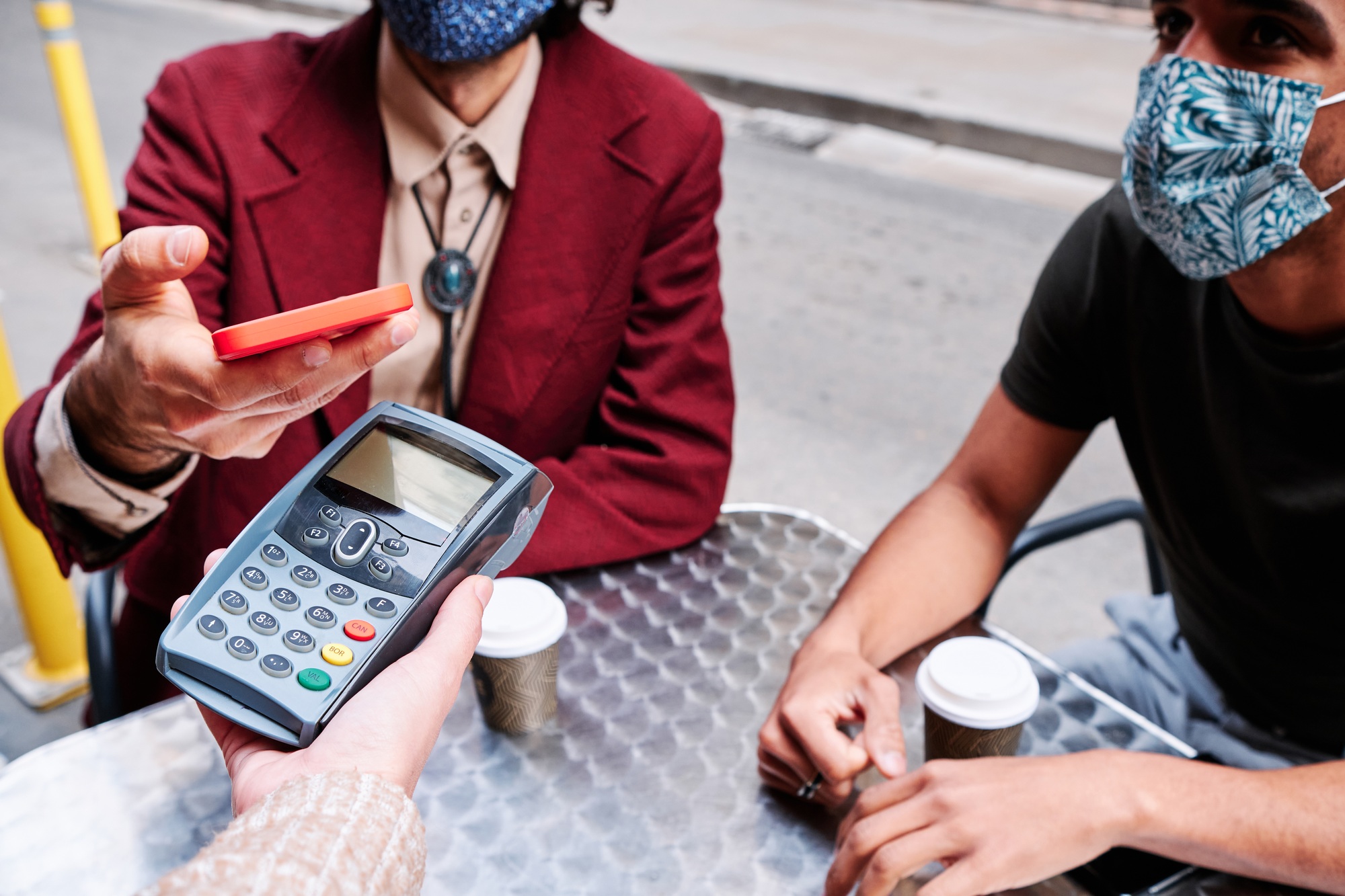 young adult man paying with mobile phone using a dataphone and waring protective mask - new normal